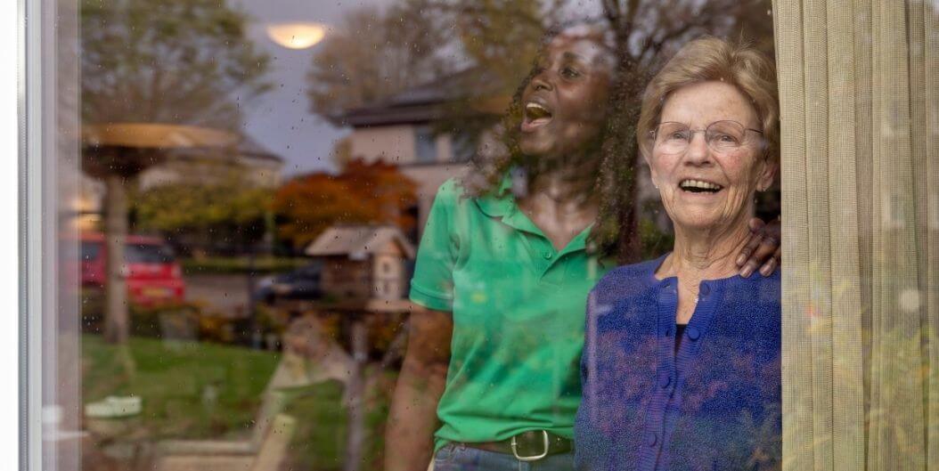 Elderly Woman With Her Female Nurse by the Windows At Independent Living Facility