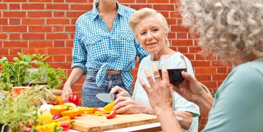 Elderly Woman Cutting Fruits and Vegetables at an Outdoor Table with Friends at an Independent Living Facility
